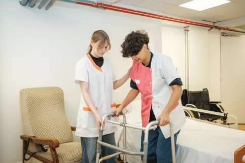 Deux jeunes en formation dans une chambre avec un lit médicalisé et un déambulateur