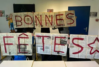 "Bonnes fêtes" est écrit sur des pages de journaux ouvertes tenues par des élèves
