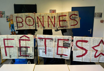 "Bonnes fêtes" est écrit sur des pages de journaux ouvertes tenues par des élèves