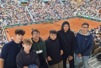 les jeunes du projet tennis sont spectateurs d'un match de tennis à Roland Garros. Ils posent devant un terrain en terre battue.