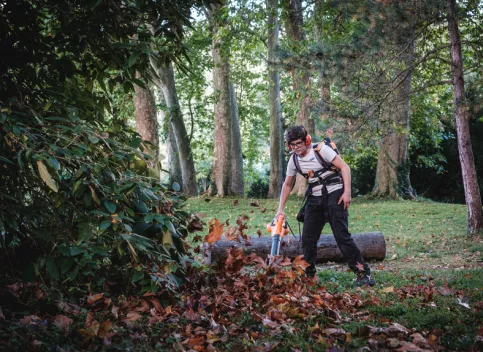 Un jeune en formation jardinier paysagiste en train de souffler les feuilles 