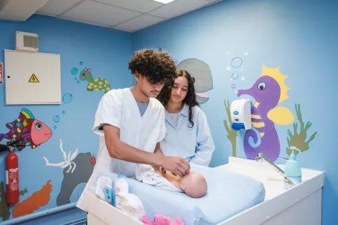 Deux jeunes en formation SAPAT s'occupent d'un bébé en salle de puériculture