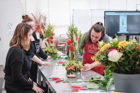 Deux jeunes en formation avec leur enseignante en train de composer un bouquet 