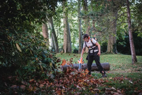 Un jeune en formation jardinier paysagiste en train de souffler les feuilles 