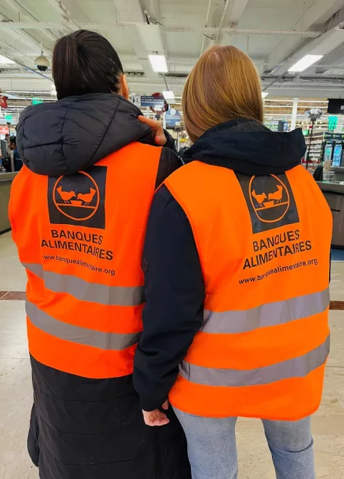 deux élèves sont de dos, on peut lire sur leur gilet orange "banque alimentaire"