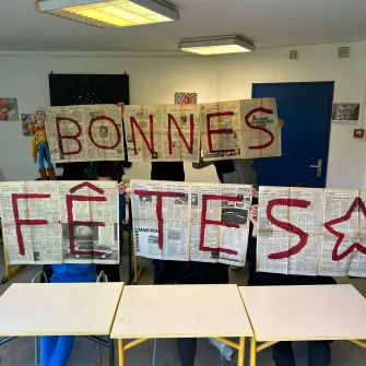 "Bonnes fêtes" est écrit sur des pages de journaux ouvertes tenues par des élèves