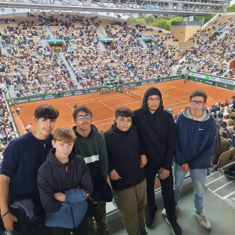 les jeunes du projet tennis sont spectateurs d'un match de tennis à Roland Garros. Ils posent devant un terrain en terre battue.